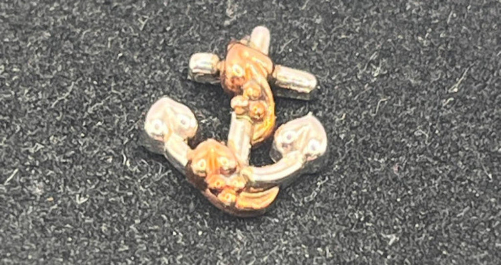 Gold and silver anchor-shaped earring on a dark textured background