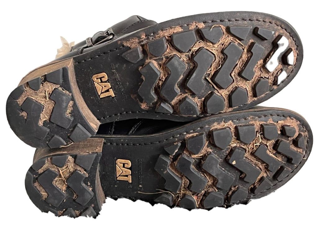 Close-up of black Cat brand shoes with tread pattern on a white background